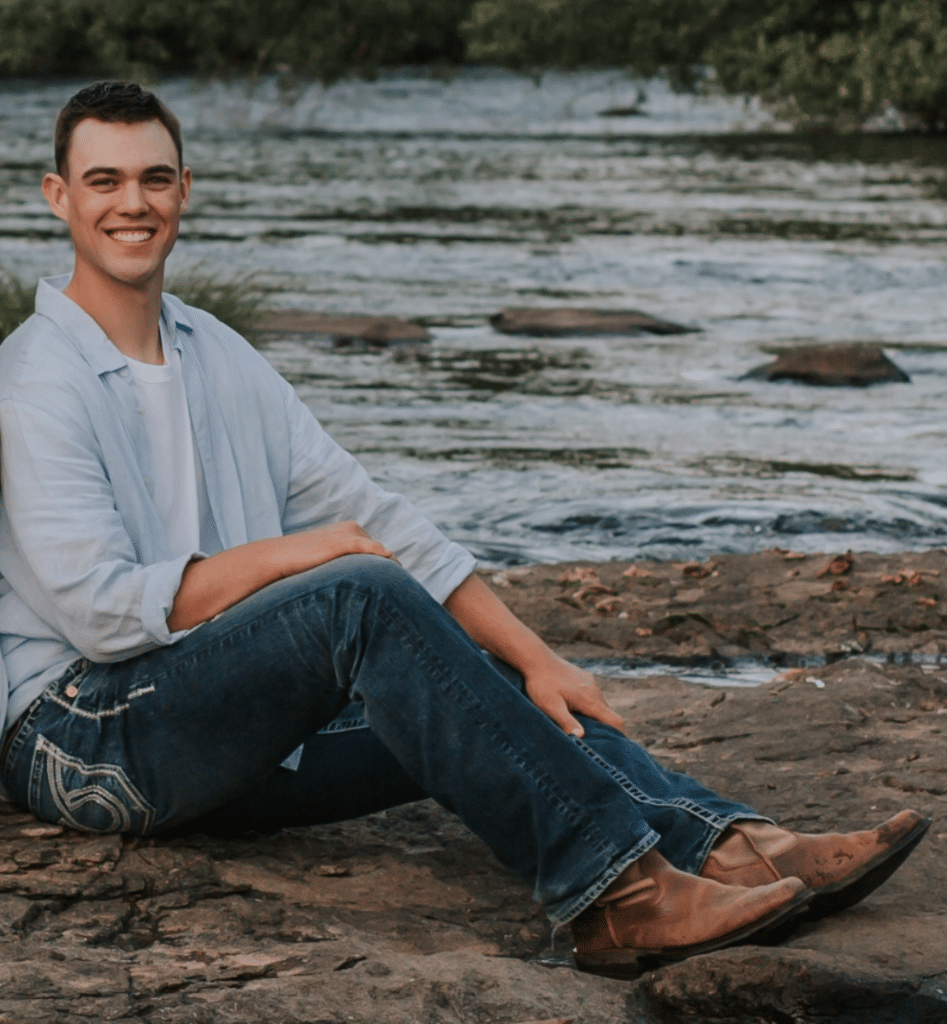 male sitting on rocks next to water