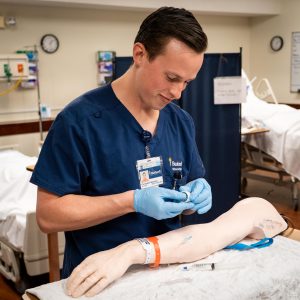 Male nursing student practicing iv with mannequin arm