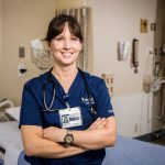 Confident nursing student in blue scrubs smiling in a clinic room