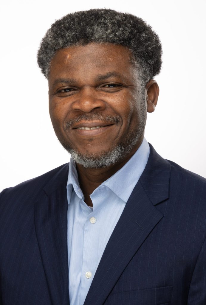Portrait of a smiling man with salt-and-pepper hair and beard wearing a navy suit and light blue collared shirt.