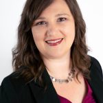 Headshot of a smiling woman with shoulder-length brown hair wearing a black blazer and maroon top, against a neutral background