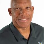 Headshot of a smiling Bushnell University track and field coach wearing a dark team polo shirt.