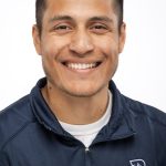 Headshot of a smiling man with short dark hair and light facial hair wearing a navy Bushnell Athletic Training jacket against a white background