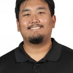 Headshot of a man with short dark hair and a goatee, wearing a black polo shirt, smiling against a white background