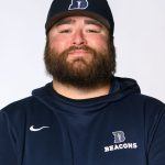 Headshot of a bearded man wearing a Bushnell Beacons baseball cap and navy Beacons hoodie, posed against a light gray background.