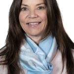 Headshot of a smiling woman with long dark brown hair wearing a light top and blue patterned scarf against a white background