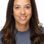 Headshot of a smiling woman with long dark brown hair wearing a gray Bushnell Beach T-shirt against a white background