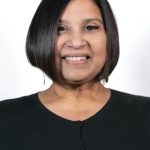Portrait of a smiling woman with short dark bob haircut wearing a black top against a light background
