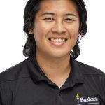 Headshot of a man with medium-length dark hair, wearing a black Bushnell Student Life polo shirt, smiling against a white background