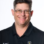 Professional headshot of man with glasses in a black polo with the Bushnell Beacons logo on it.