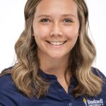 Headshot of a woman with shoulder-length wavy blonde hair, wearing a navy Bushnell University top, smiling against a white background