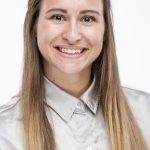 Headshot of a smiling woman with long light brown hair wearing a light gray button-up shirt against a white background
