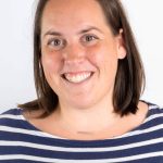 Portrait of a smiling woman with brown hair wearing a navy and white striped shirt against a light background.