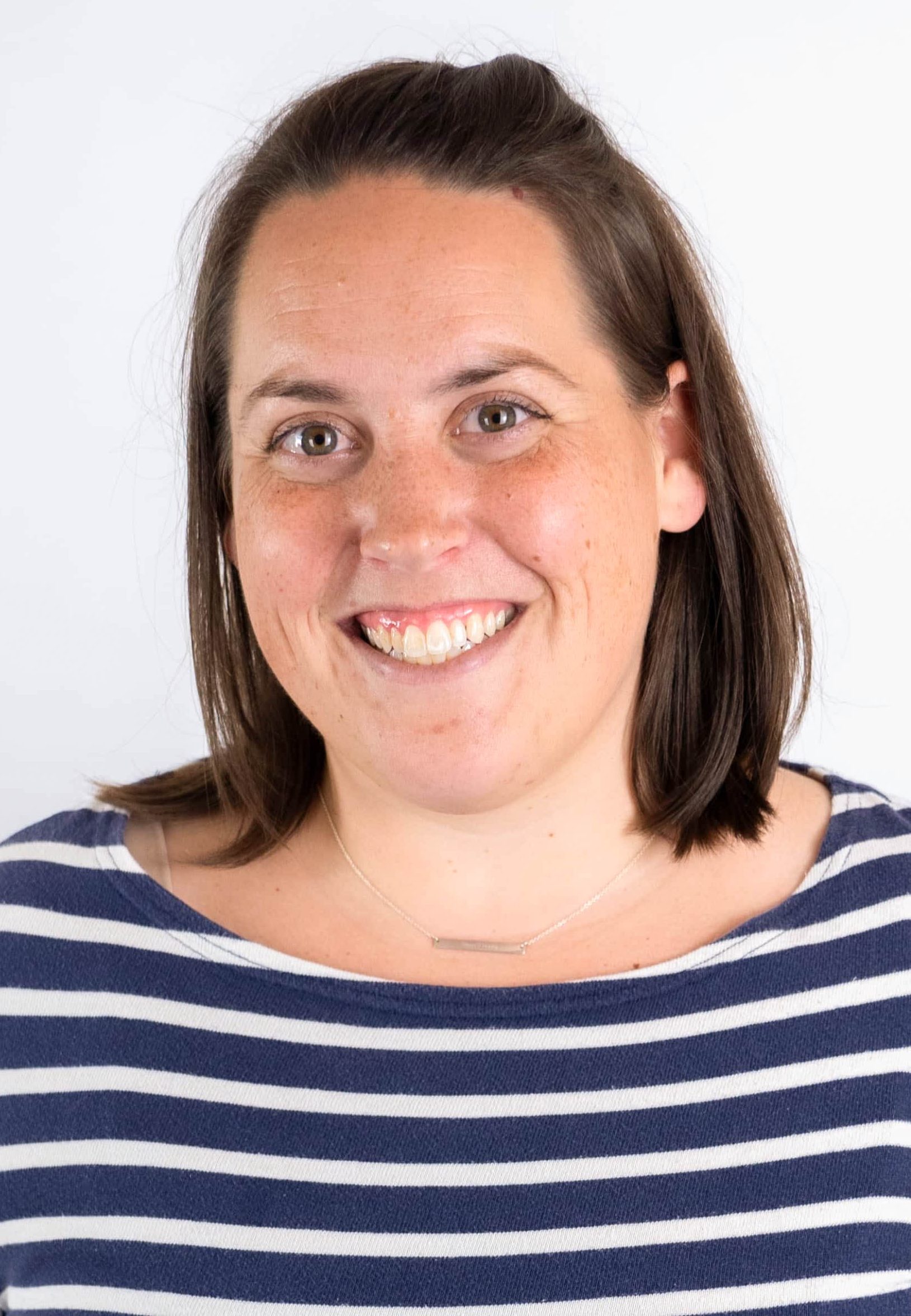 Portrait of a smiling woman with brown hair wearing a navy and white striped shirt against a light background.