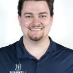 Headshot of a man with dark hair and a short goatee wearing a navy Bushnell polo, smiling against a white background