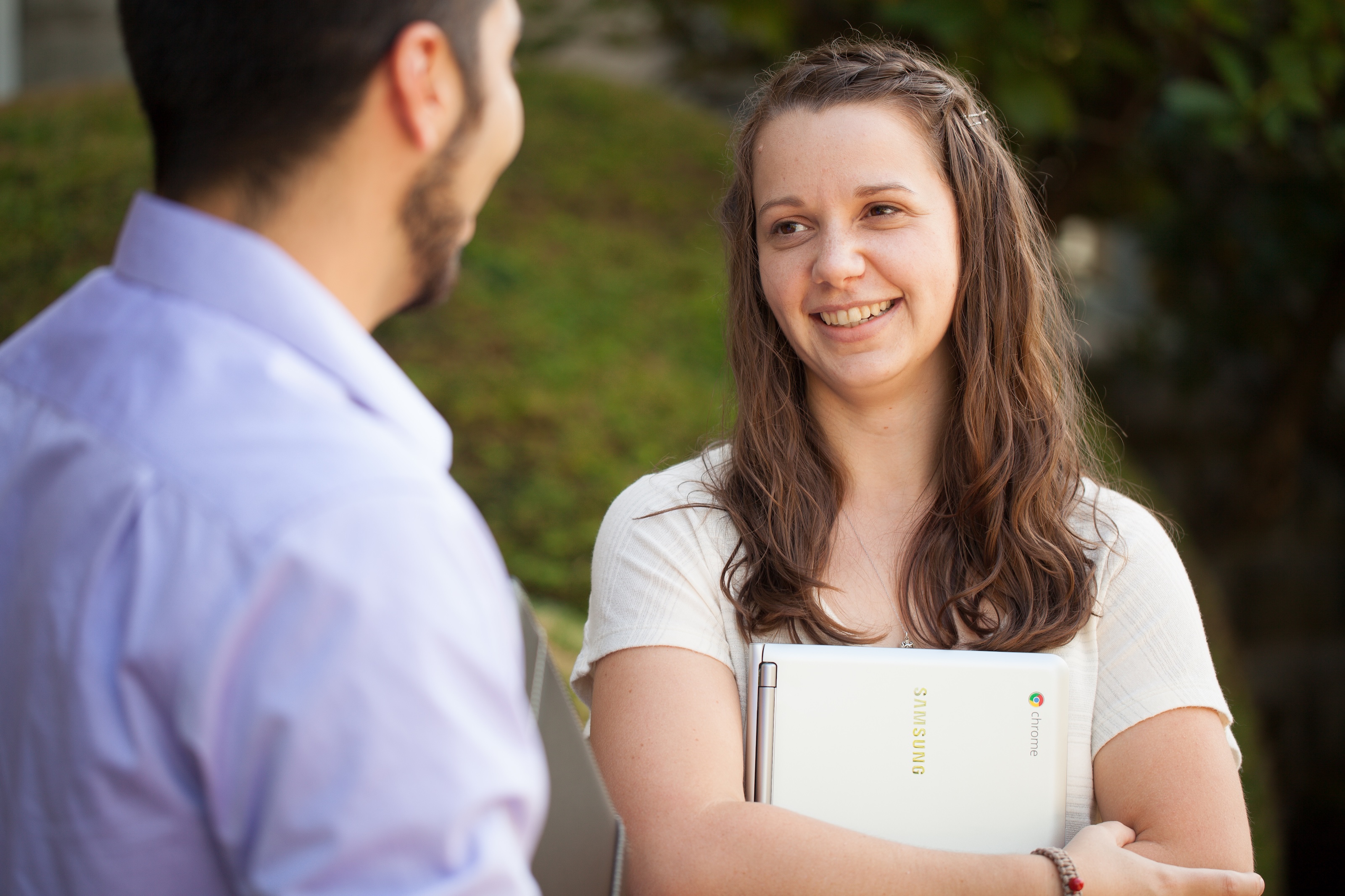 Two Bushnell University students talking together outside while holding laptops.