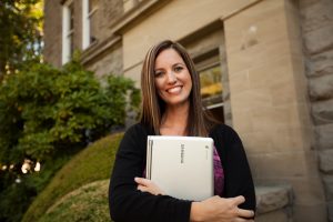 Student holds a laptop while standing outside a campus building.