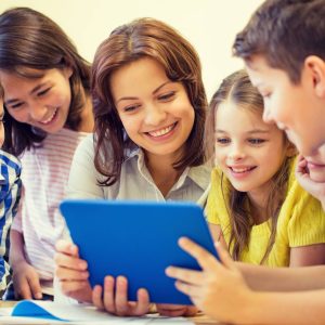 Teacher helping elementary students learn together using a tablet in the classroom.