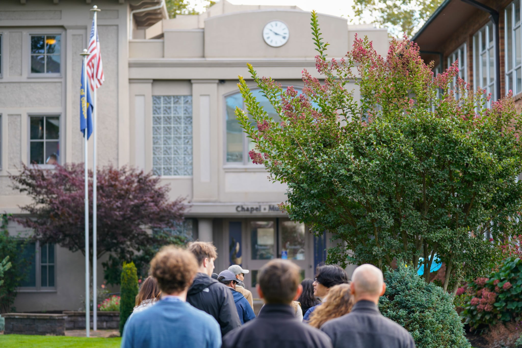 Students walking towards a campus building with a flagpole next to it