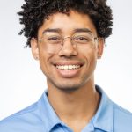Headshot of a smiling man with short curly hair and glasses, wearing a light blue polo shirt against a white background