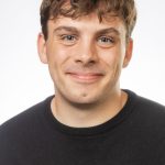 Headshot of a smiling man with short curly brown hair wearing a black Bushnell University sweater against a white background