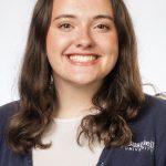 Headshot of a smiling woman with shoulder-length brown hair, wearing a navy Bushnell University cardigan over a white top against a white background