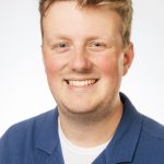 Headshot of a smiling man with short light brown hair wearing a blue collared shirt against a white background