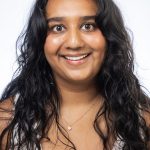 Headshot of a smiling woman with long dark wavy hair wearing a white top against a white background