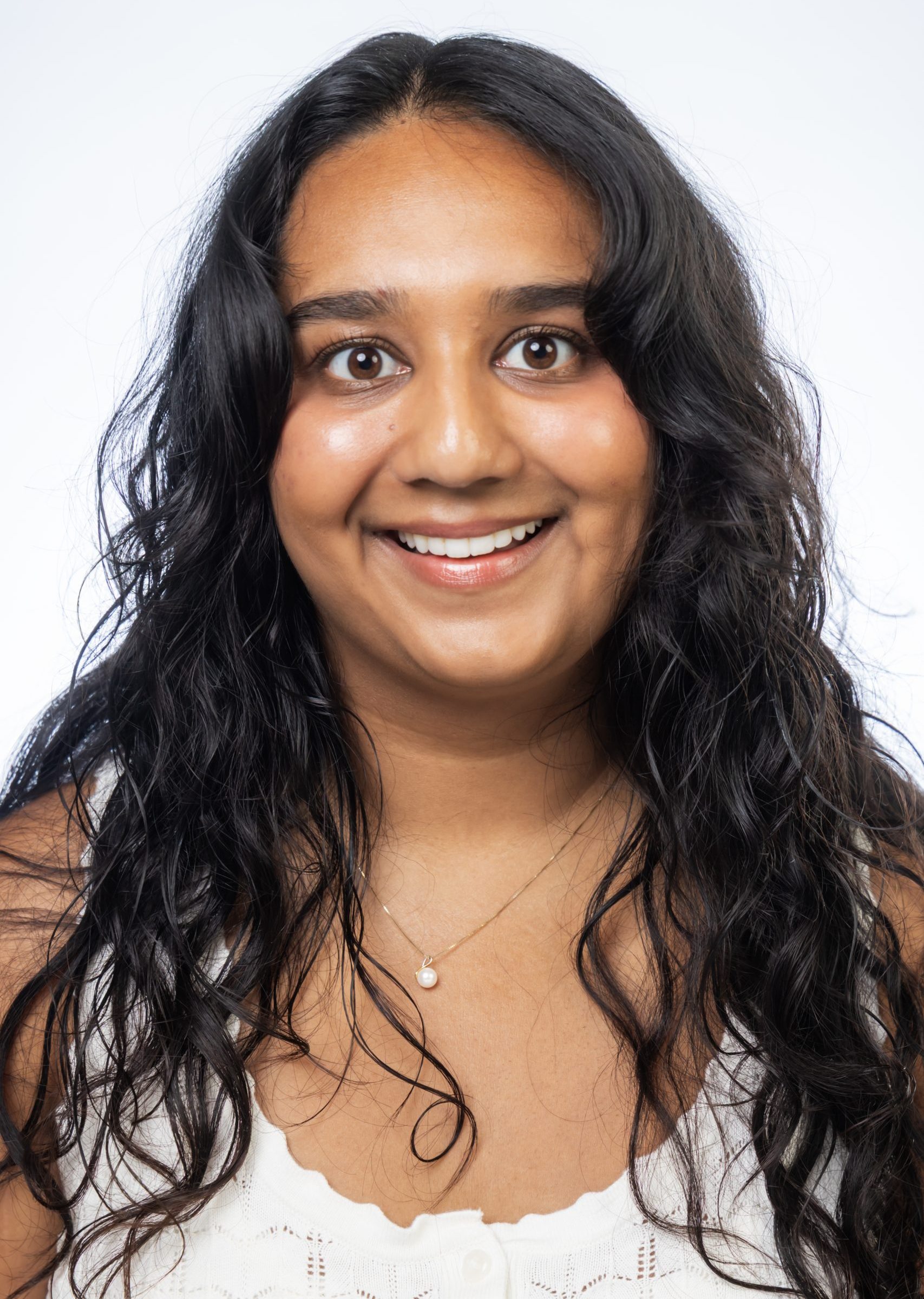 Headshot of a smiling woman with long dark wavy hair wearing a white top against a white background