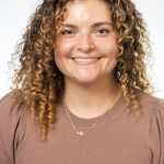 Headshot of a smiling woman with curly light brown hair wearing a brown top against a white background