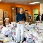 Bushnell University student standing in a donation collection center surrounded by boxes and bags of donated items while organizing a community service project.