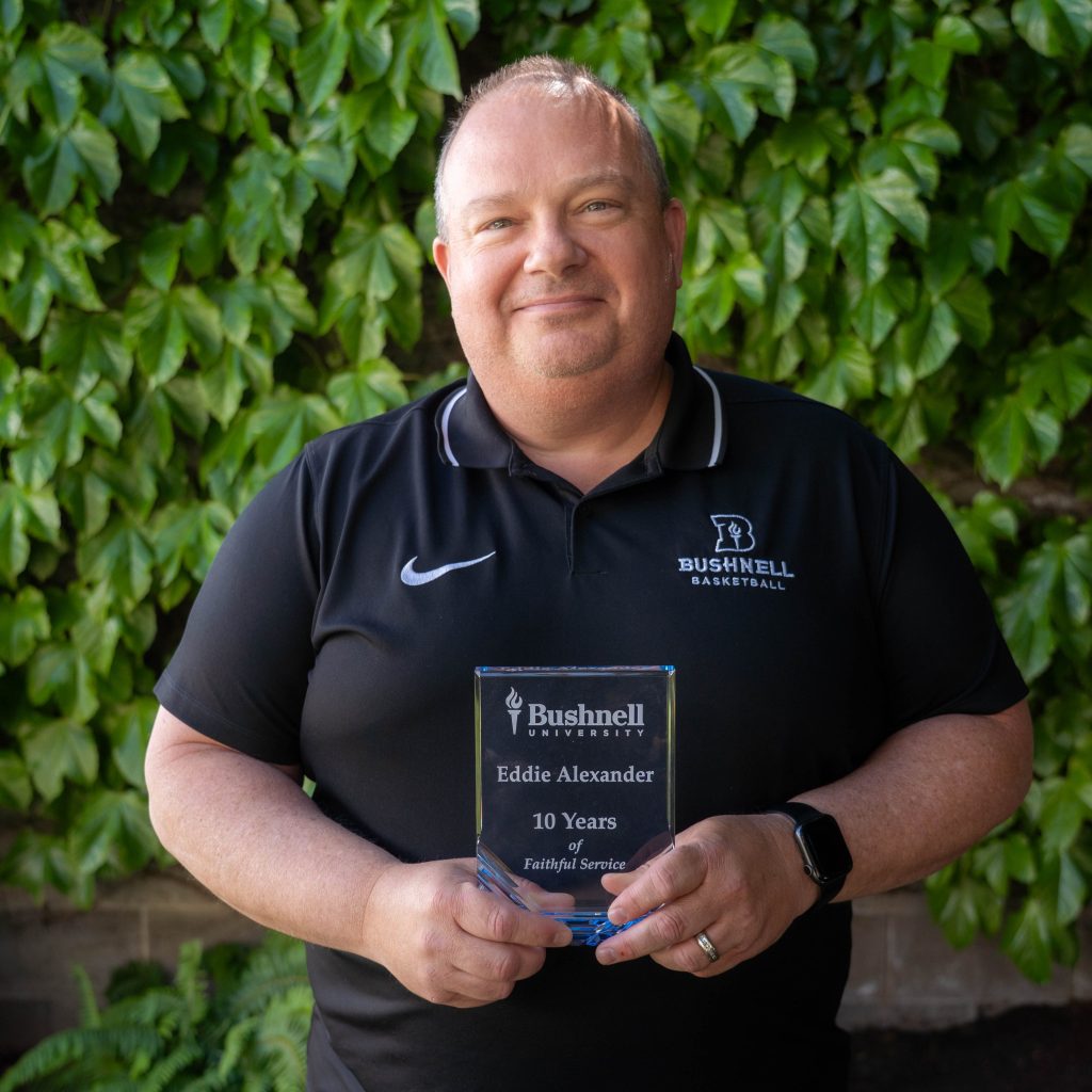 Employee recognized for 10 years of faithful service while holding a commemorative award outdoors on campus