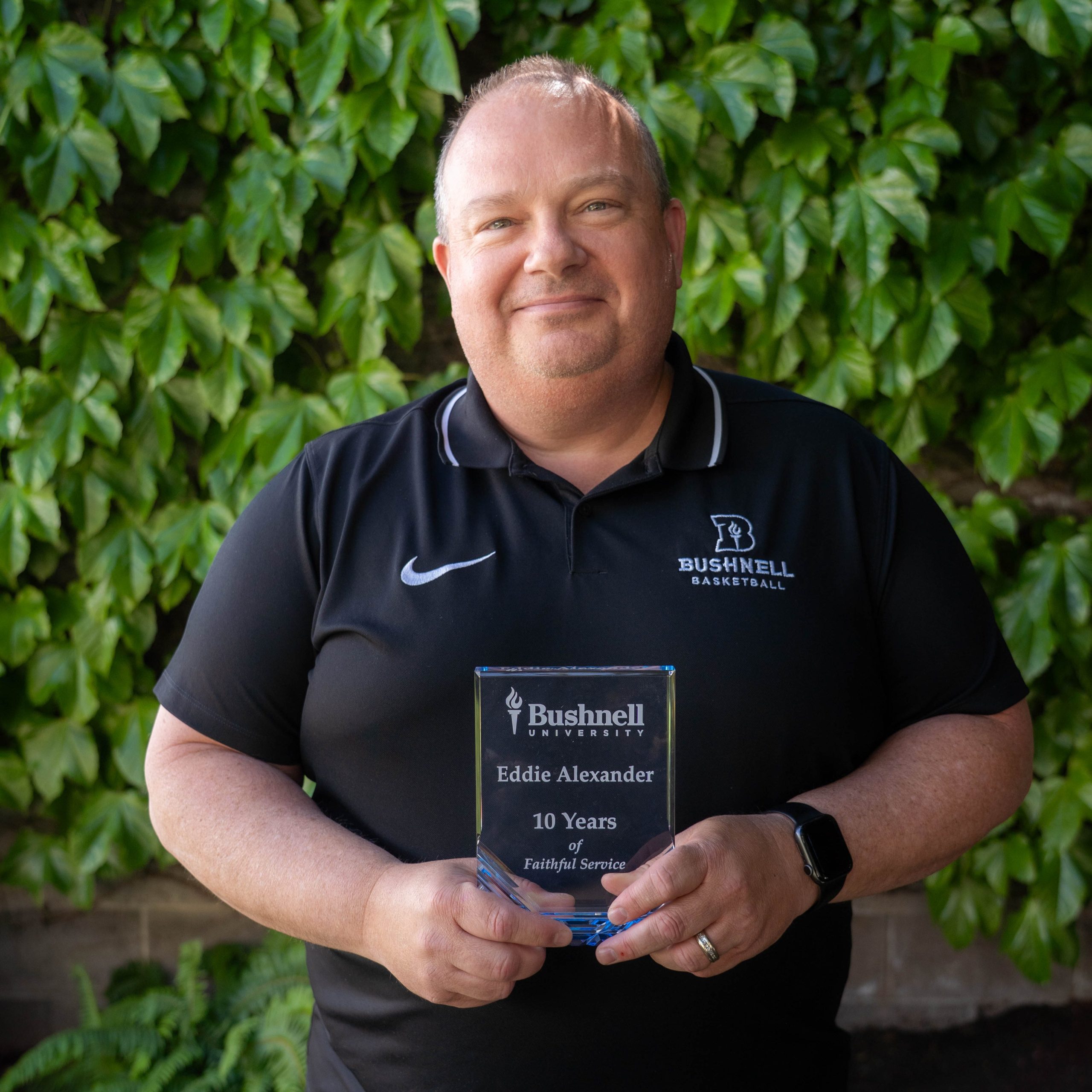 Employee recognized for 10 years of faithful service while holding a commemorative award outdoors on campus
