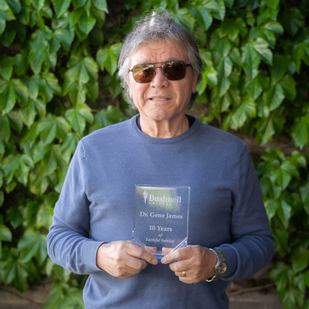 Employee recognized for 10 years of faithful service while holding a commemorative award outdoors on campus