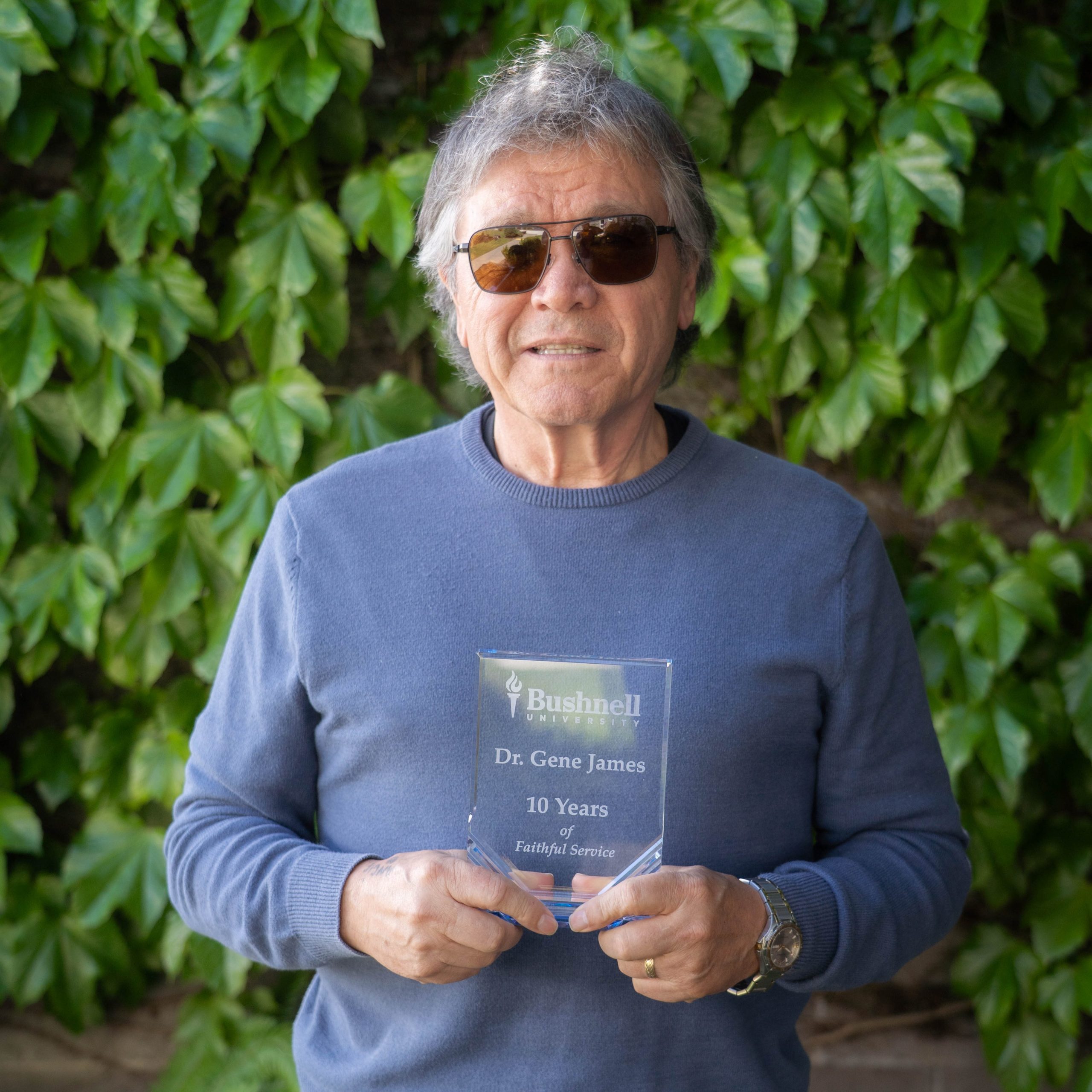 Employee recognized for 10 years of faithful service while holding a commemorative award outdoors on campus