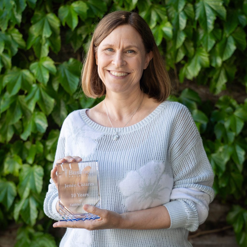 Employee recognized for 10 years of faithful service while holding a commemorative award outdoors on campus