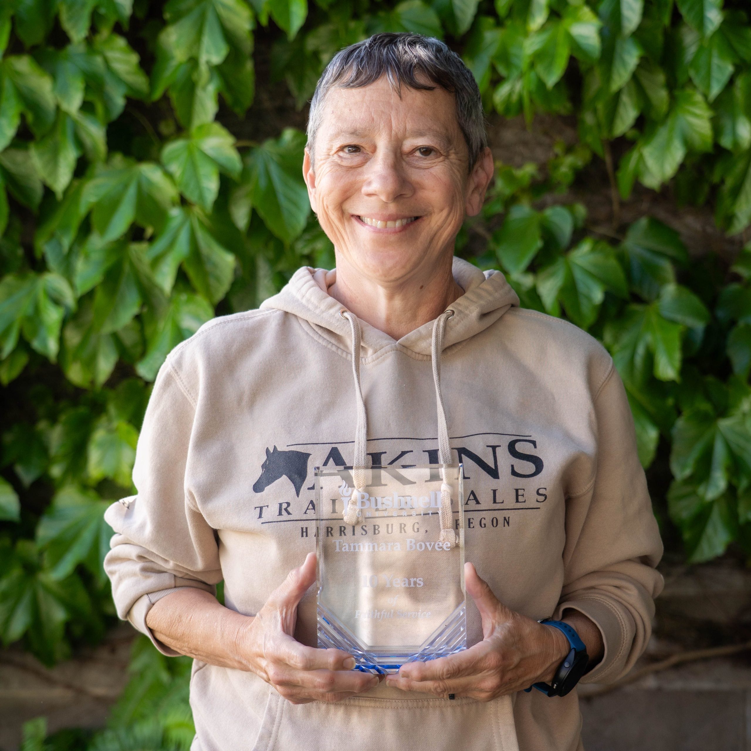 Employee recognized for 10 years of faithful service while holding a commemorative award outdoors on campus