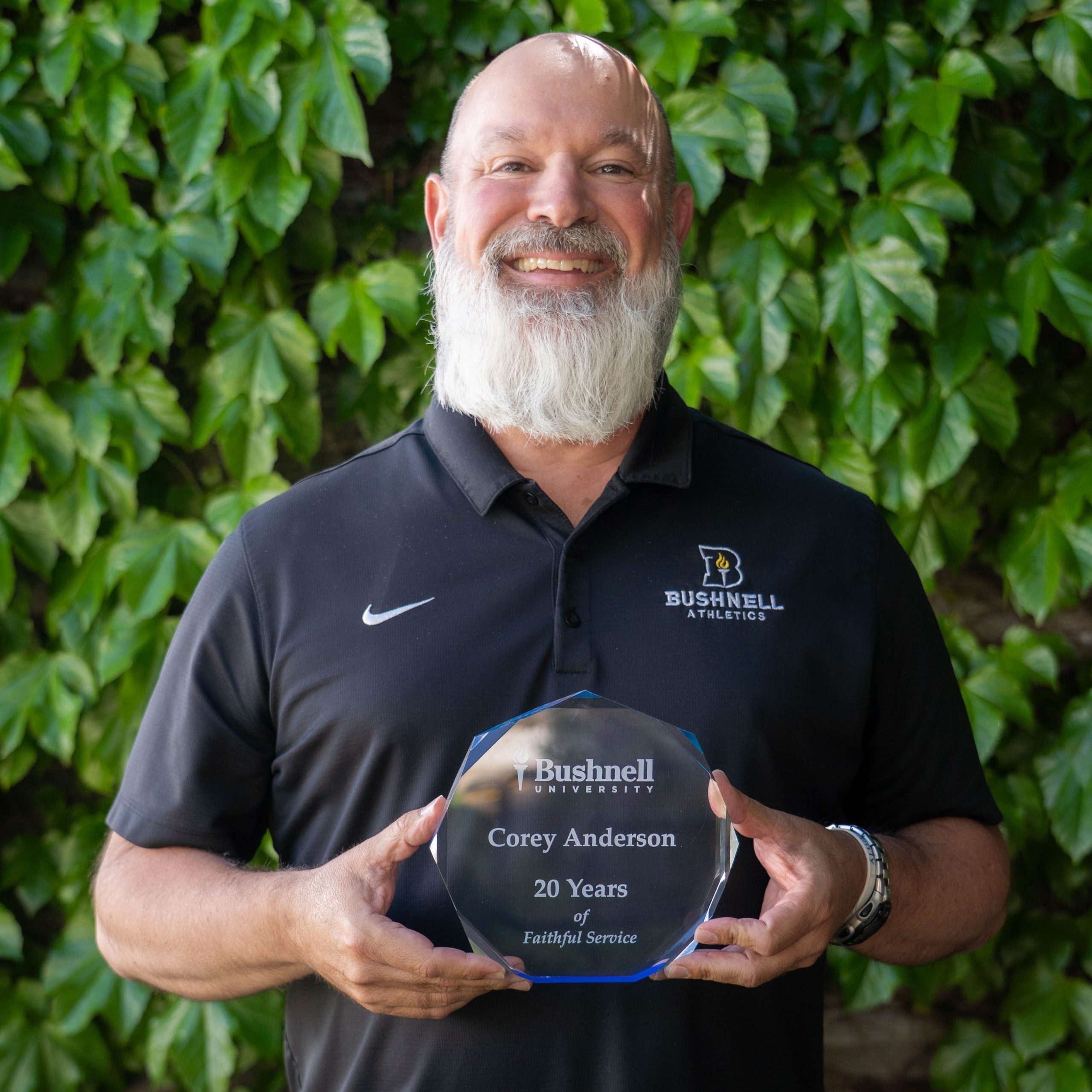 Employee recognized for 20 years of faithful service while holding a commemorative award outdoors on campus