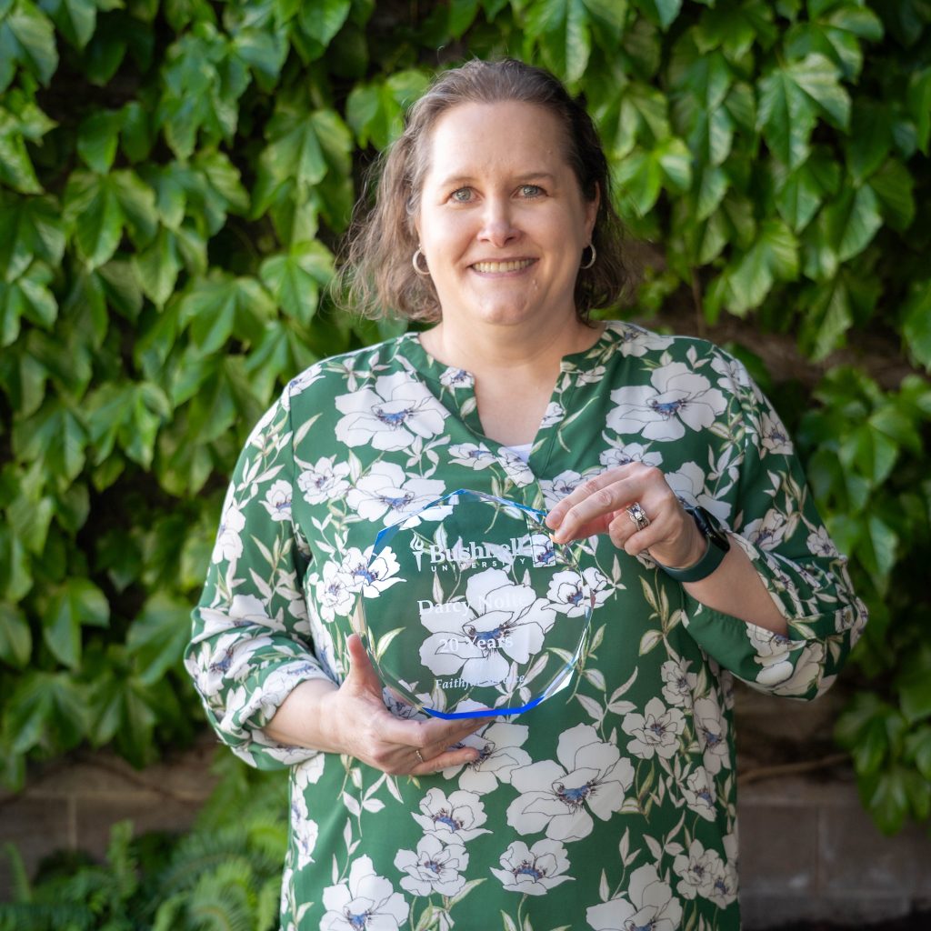 Employee recognized for 20 years of faithful service while holding a commemorative award outdoors on campus