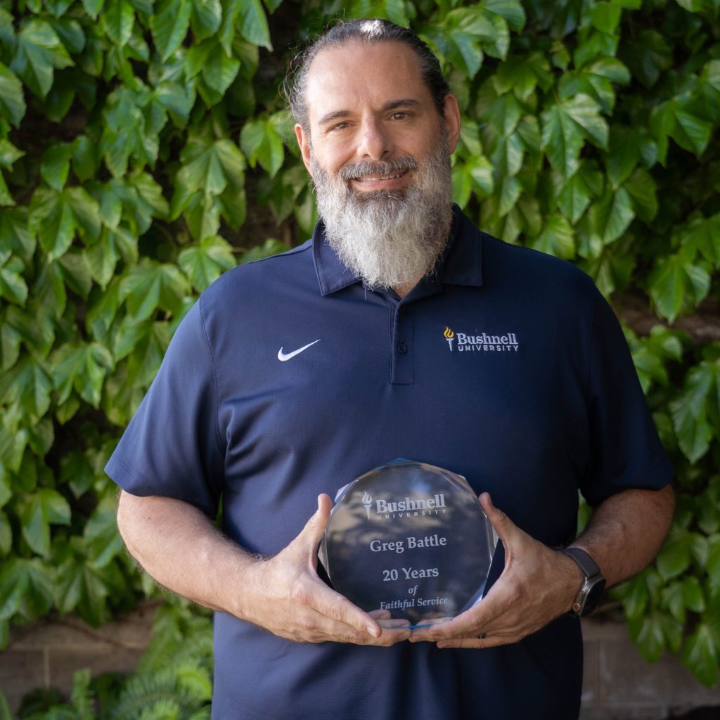 Employee recognized for 20 years of faithful service while holding a commemorative award outdoors on campus