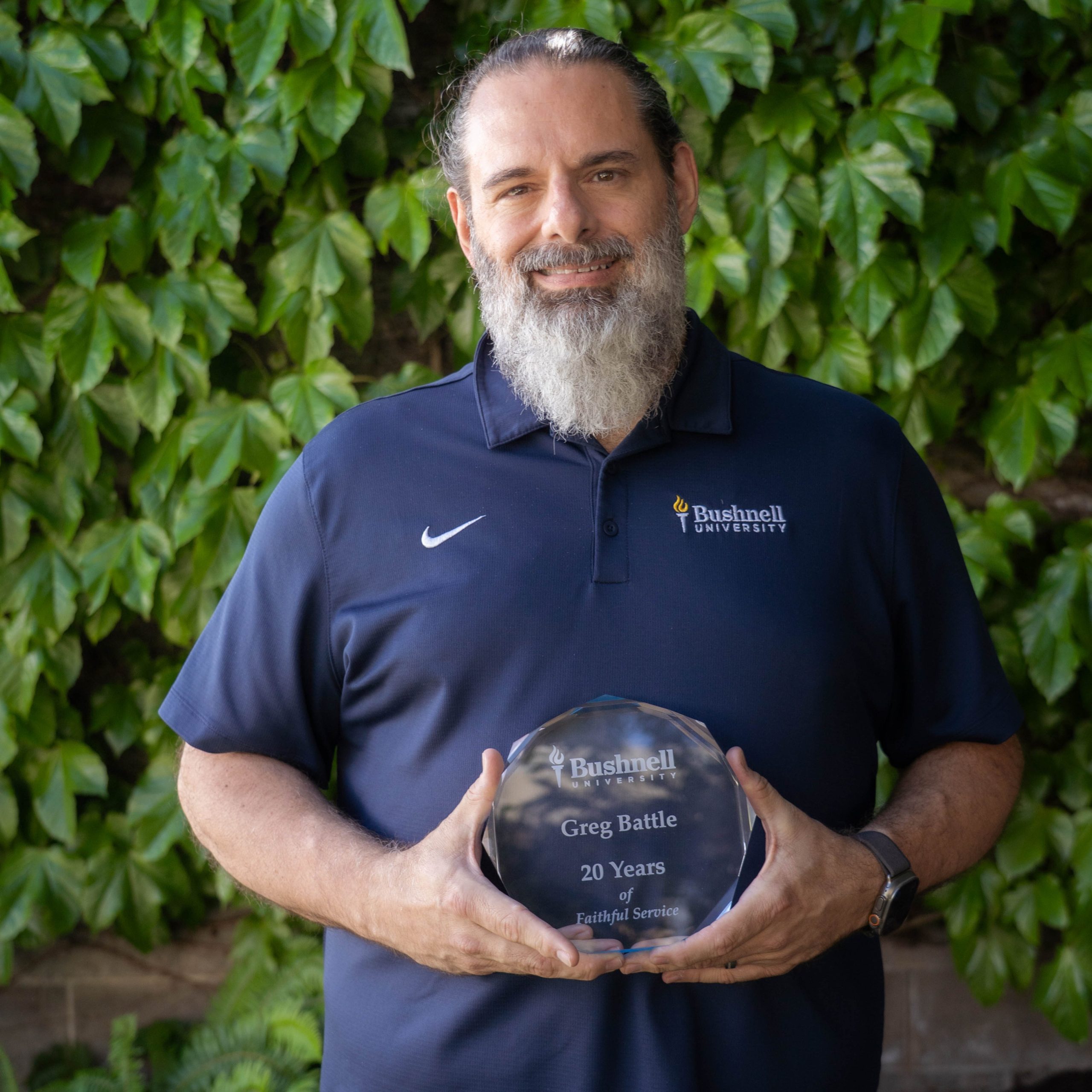 Employee recognized for 20 years of faithful service while holding a commemorative award outdoors on campus