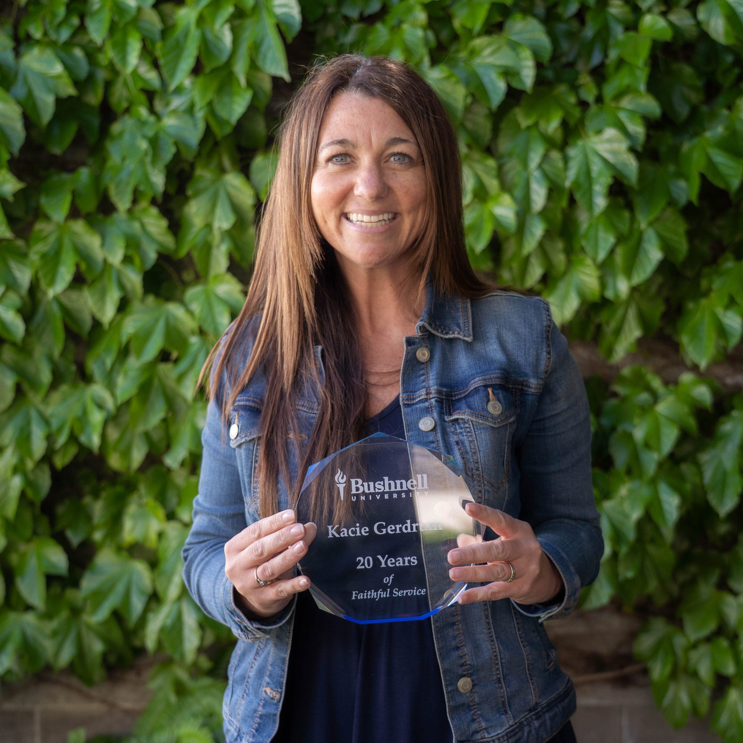 Employee recognized for 20 years of faithful service while holding a commemorative award outdoors on campus