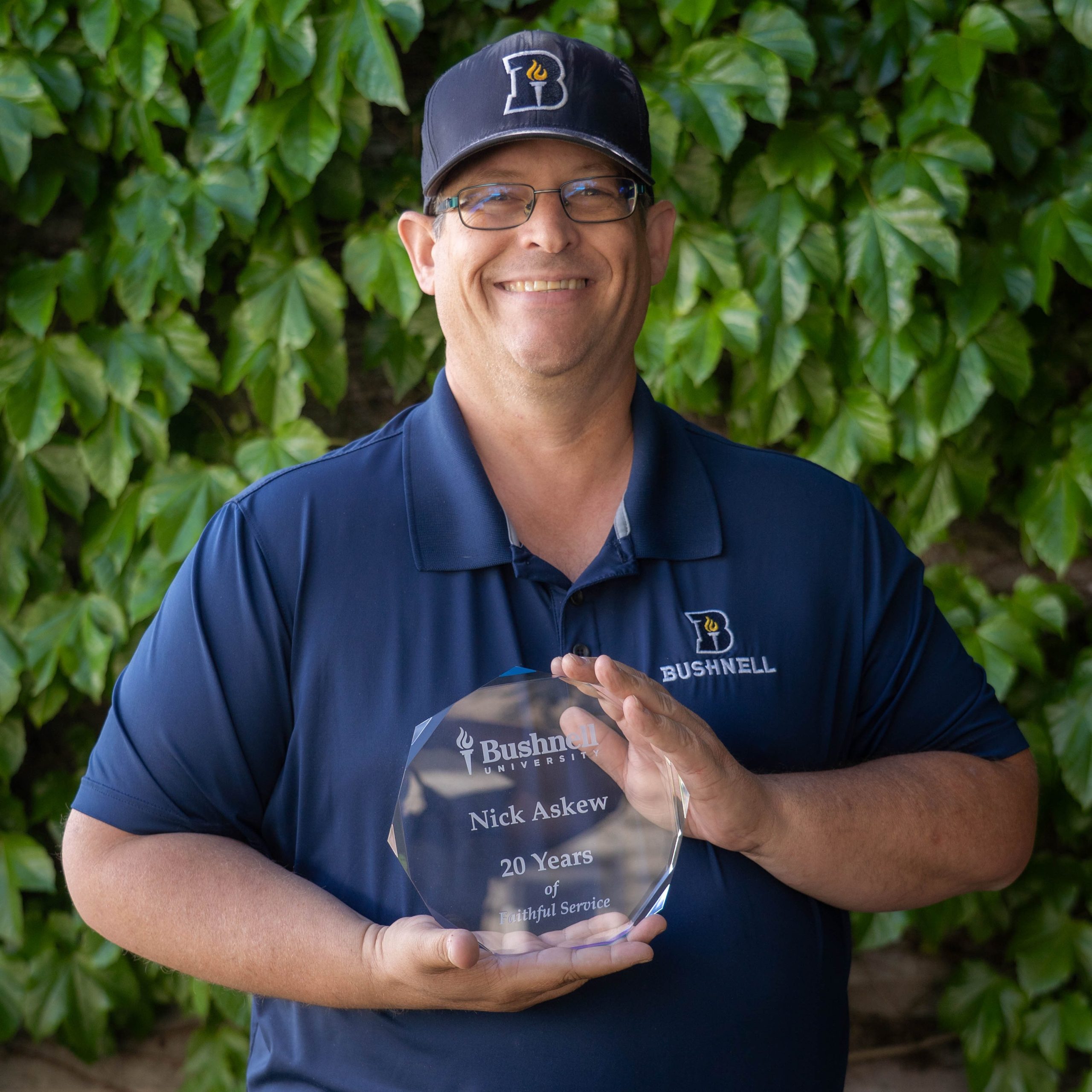 Employee recognized for 20 years of faithful service while holding a commemorative award outdoors on campus