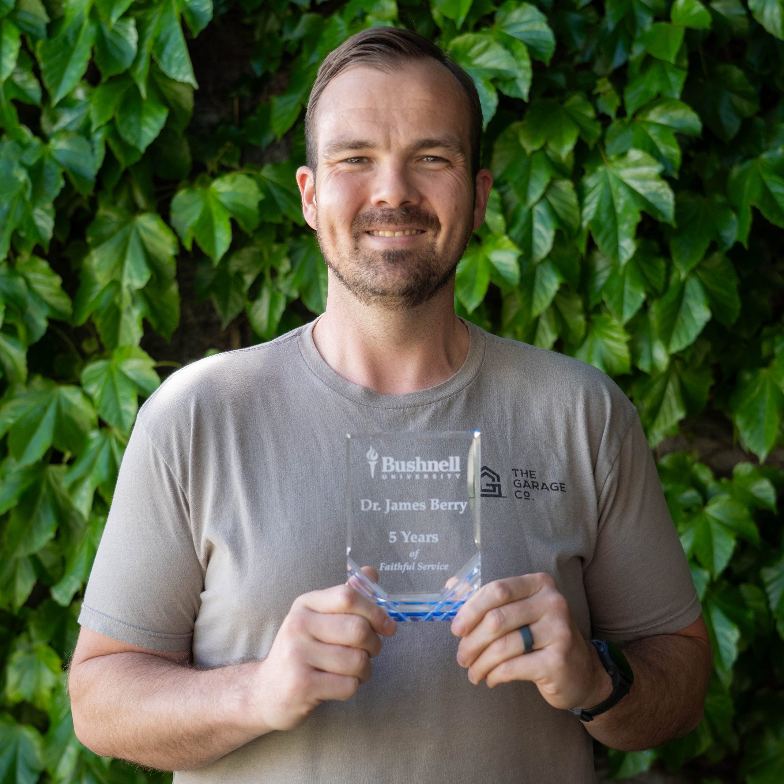 Employee recognized for 5 years of faithful service while holding a commemorative award outdoors on campus