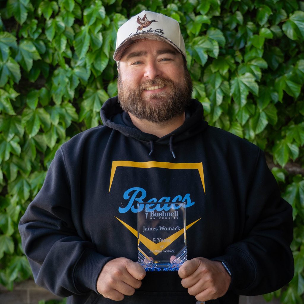 Employee recognized for 5 years of faithful service while holding a commemorative award outdoors on campus