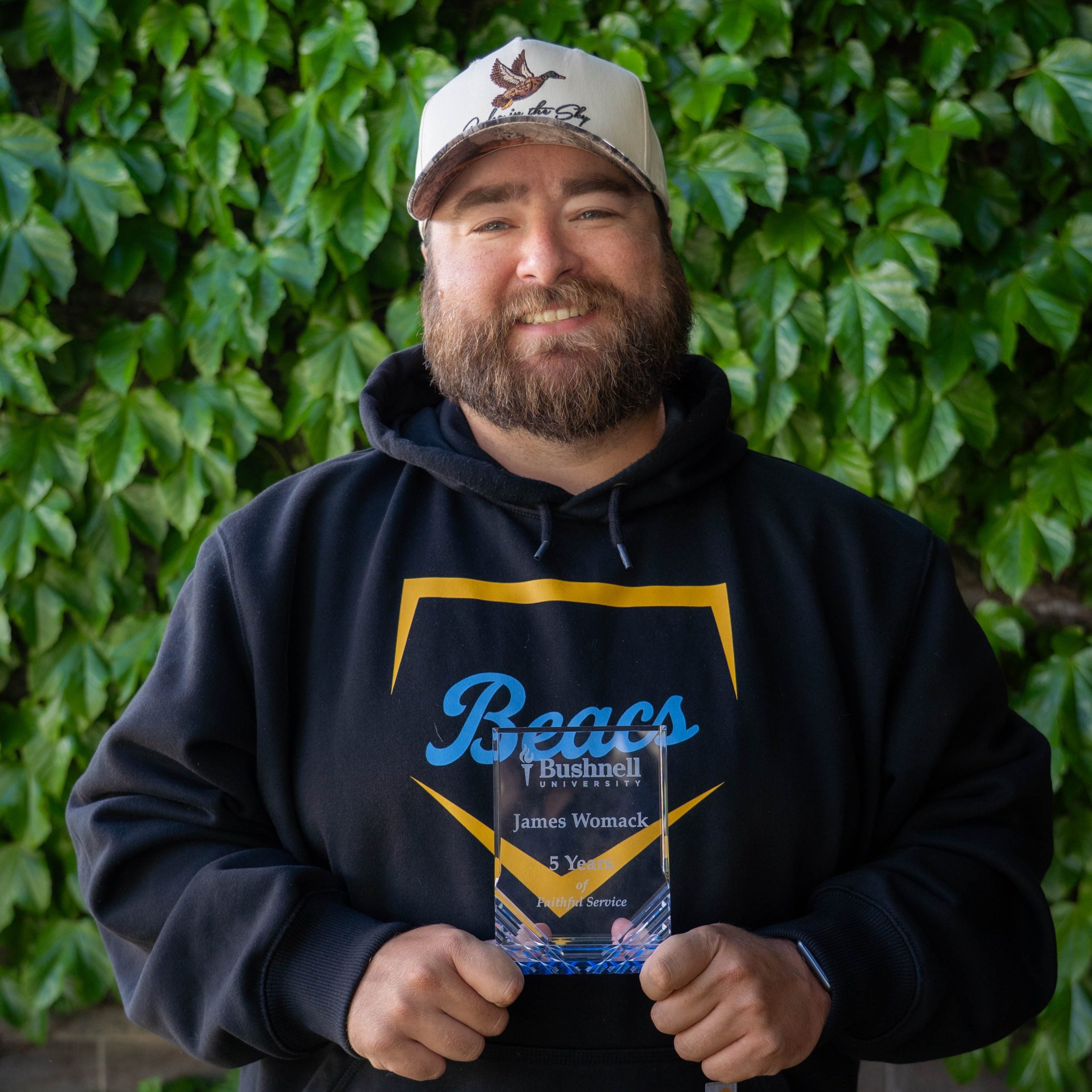 Employee recognized for 5 years of faithful service while holding a commemorative award outdoors on campus