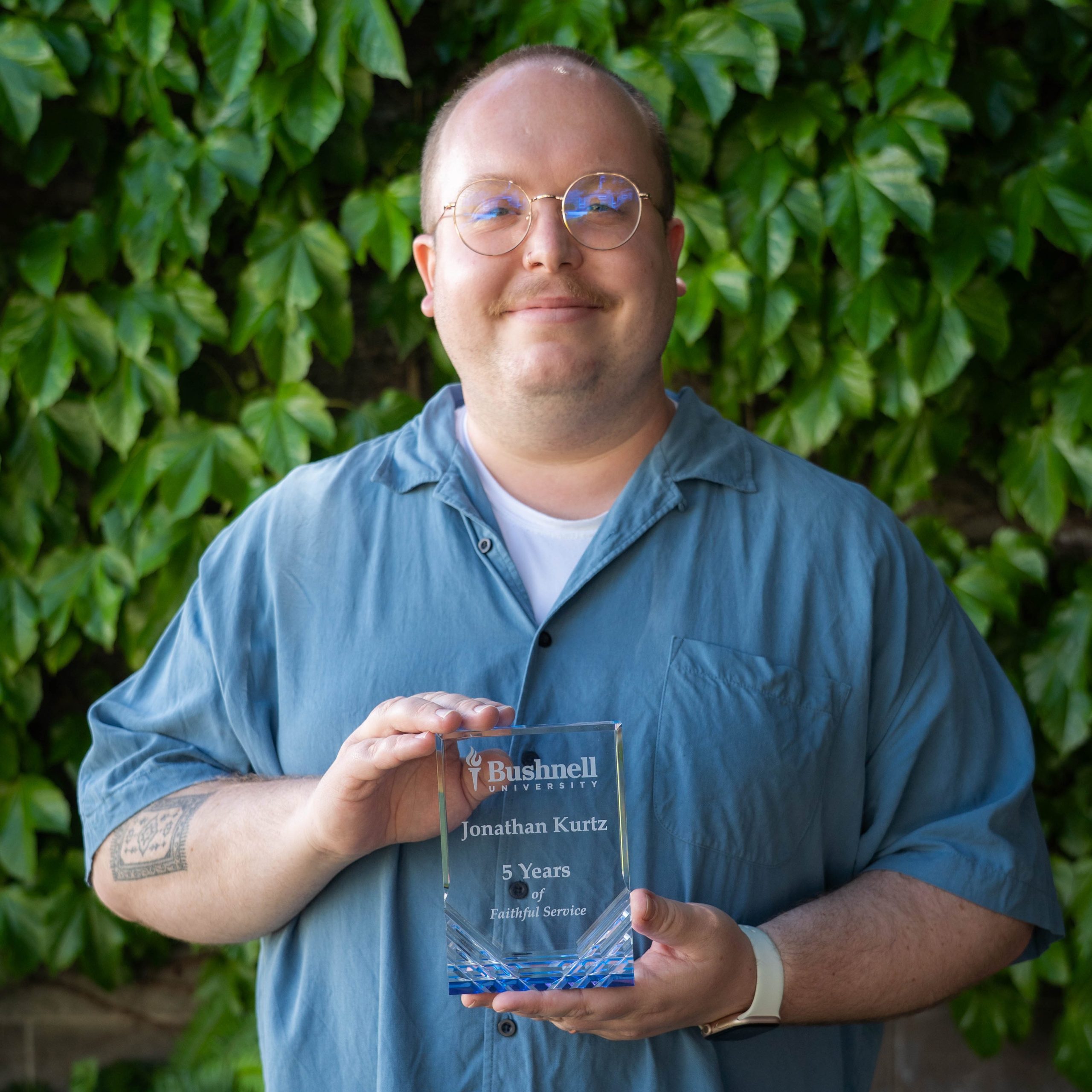 Employee recognized for 5 years of faithful service while holding a commemorative award outdoors on campus