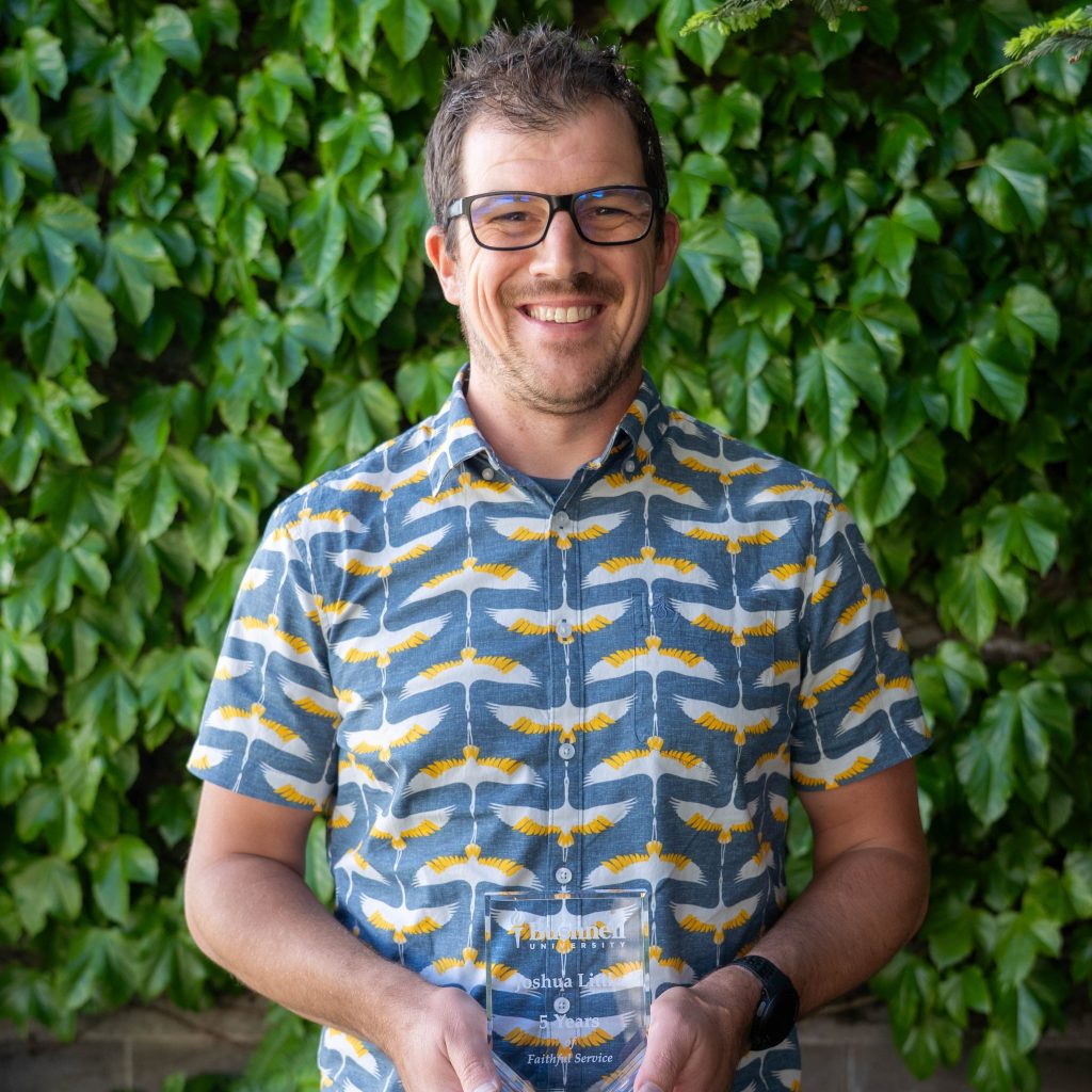 Employee recognized for 5 years of faithful service while holding a commemorative award outdoors on campus