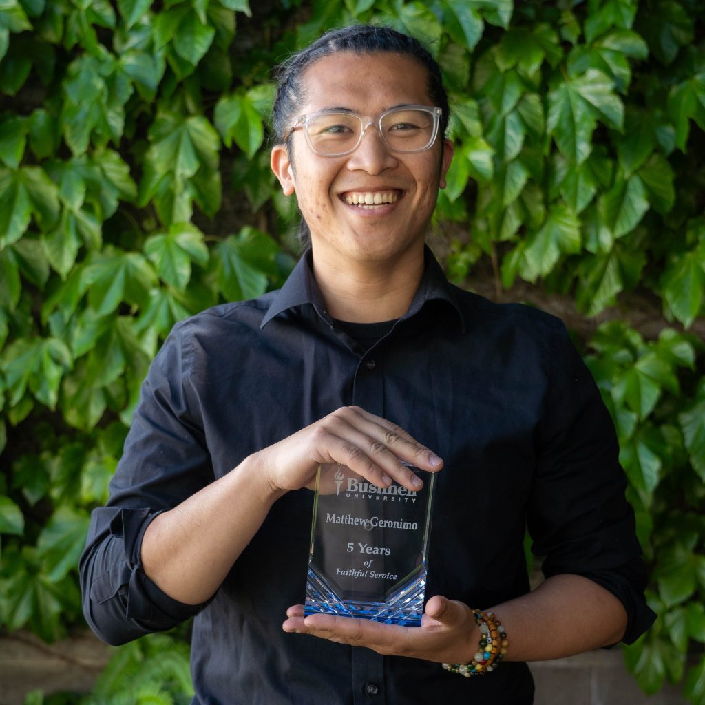Employee recognized for 5 years of faithful service while holding a commemorative award outdoors on campus