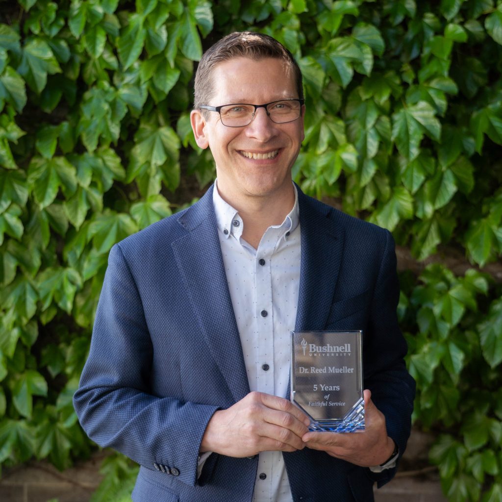 Employee recognized for 5 years of faithful service while holding a commemorative award outdoors on campus